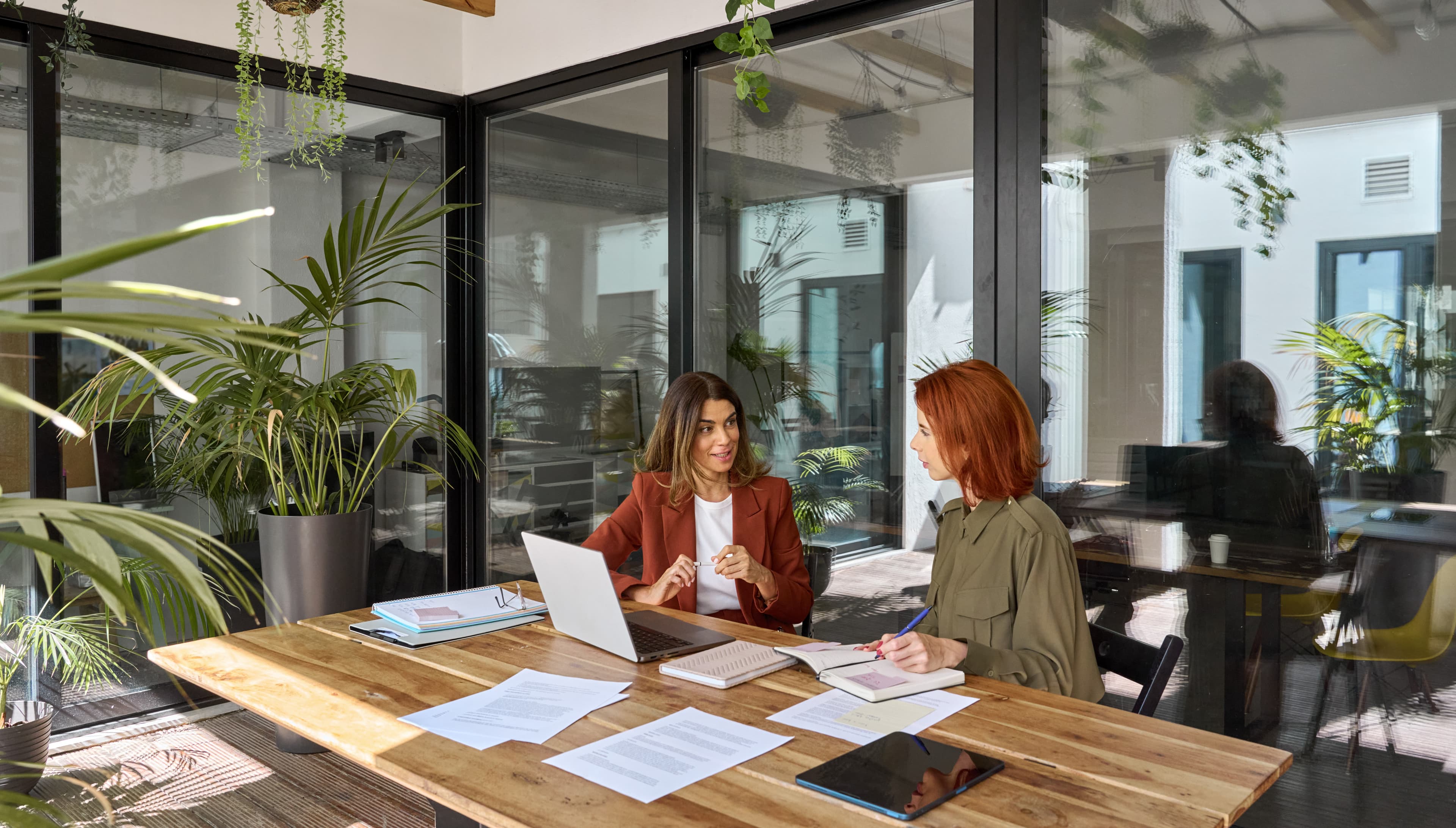 Three people seated at a table having a business discussion in a sunlit office.