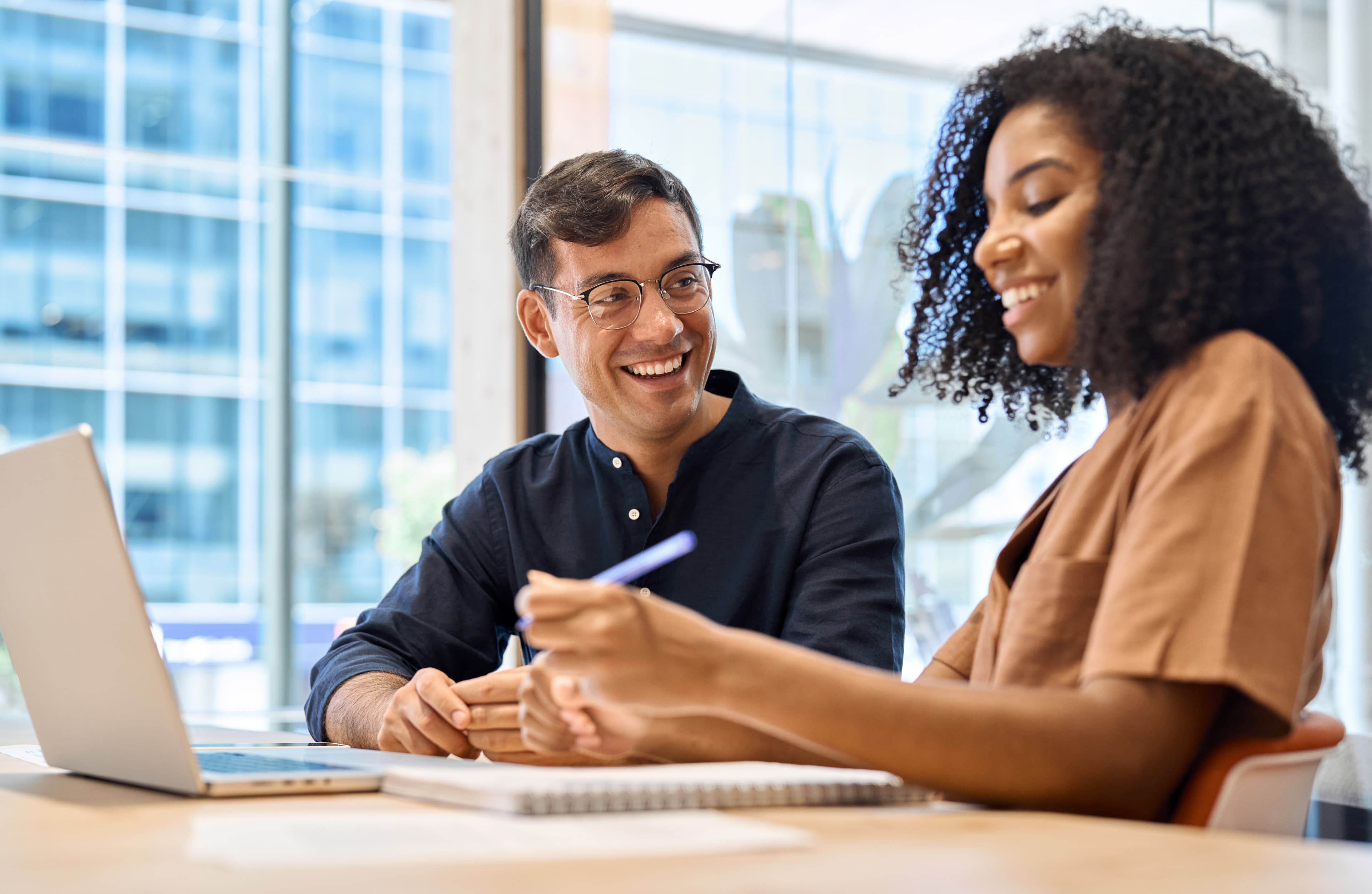 Man and woman smiling while discussing something on a laptop.